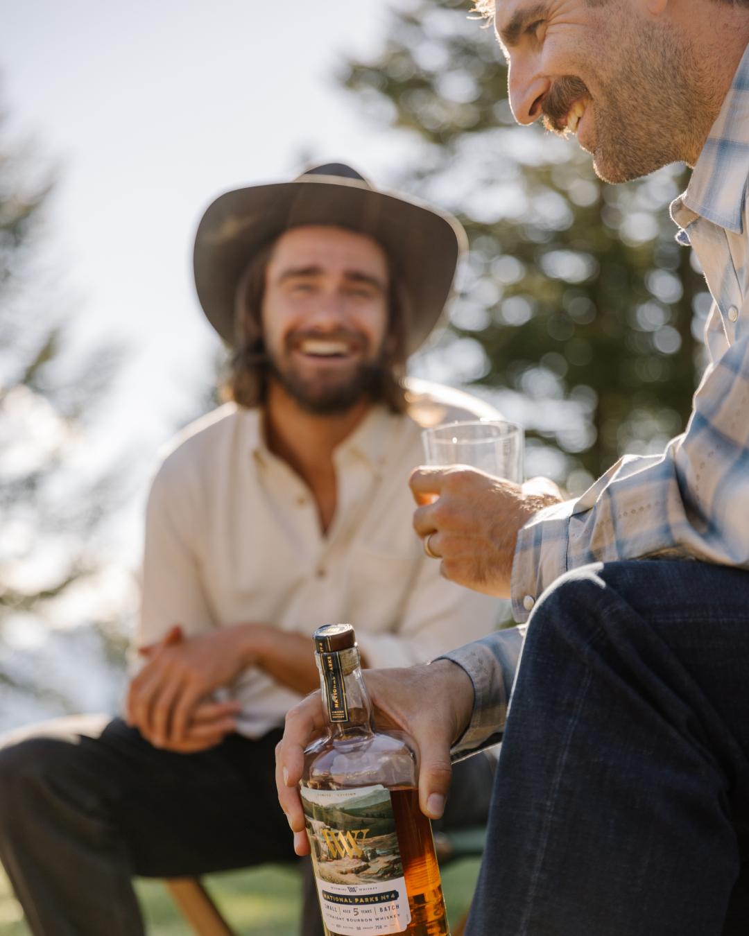 Two men, one in a cowboy hat, holding glasses of Wyoming whisky